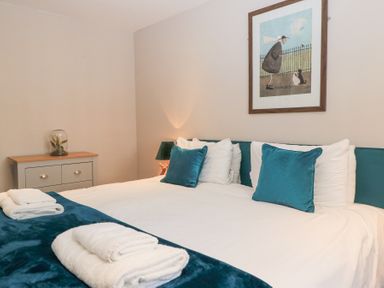 A bedroom with a bed with teal pillows and white linens and towels on the teal bed runner at Mayfield Cottage Nr Malmesbury