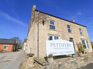 The exterior of Pettifers Freehouse Hotel with a sign in front and stone buildings around Nr Malmesbury