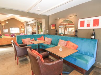 A dining area with blue upholstered bench seating orange and patterned cushions and brown leather chairs at Mayfield Cottage in Nr Malmesbury