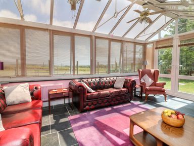 A conservatory with red leather sofas armchair wooden tables and a fruit bowl at The Old Forge Cottage in Kilkhampton