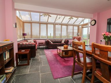A living room with leather sofas wooden coffee table and dining chairs at The Old Forge Cottage in Kilkhampton