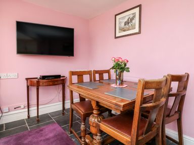 A dining area with wooden table and chairs a wall-mounted tv and a small wooden side table with a device at The Old Forge Cottage Kilkhampton
