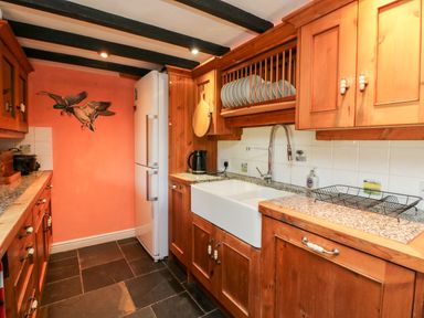 A kitchen with wooden cabinets a white refrigerator a white farmhouse sink and a dish rack at The Old Forge Cottage in Kilkhampton