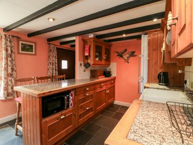 A kitchen with wooden cabinets granite countertops a microwave and a sink at The Old Forge Cottage in Kilkhampton