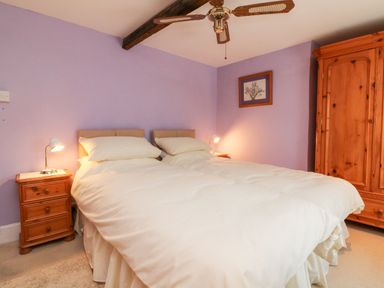 A bedroom with two single beds pushed together bedside tables with lamps a wooden wardrobe and a ceiling fan at The Old Forge Cottage in Kilkhampton