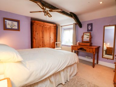 A bedroom with a bed a wooden wardrobe a wooden dressing table and a wall mirror at The Old Forge Cottage in Kilkhampton