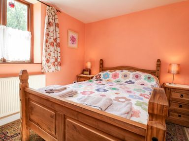 A bedroom with a wooden bed and colorful quilt next to two bedside tables with lamps at The Old Forge Cottage in Kilkhampton