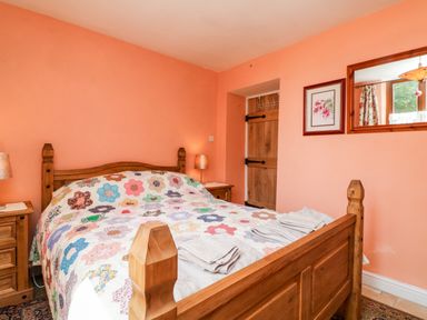A bedroom with a wooden bed frame and colorful quilt two bedside tables with lamps a wooden door a framed picture and a wall mirror at The Old Forge Cottage Kilkhampton
