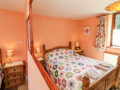 A bedroom with a wooden bed with a floral quilt and towels on top next to a window with floral curtains at The Old Forge Cottage in Kilkhampton