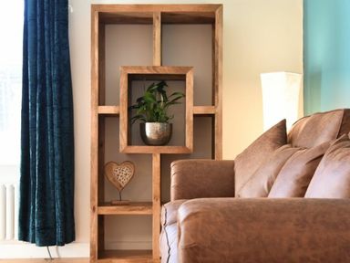 A wooden shelf with a plant and a heart decoration beside a brown sofa and a floor lamp in a living room at The Loft (Amble) in Amble