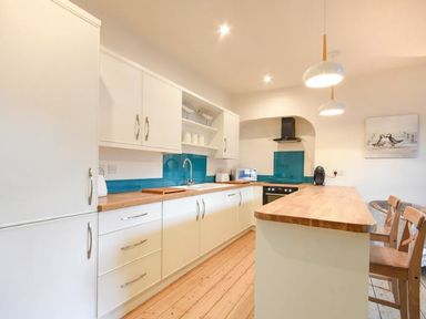 A kitchen with white cabinets wooden countertops blue backsplash and wooden bar stools at The Loft (Amble) in Amble