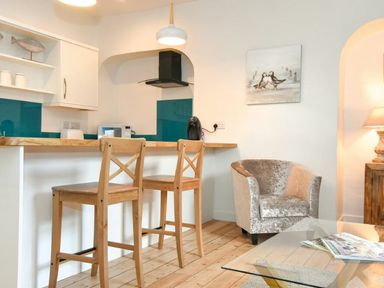 A kitchen area with two wooden bar stools a countertop with appliances and a gray armchair next to a glass coffee table at The Loft Amble