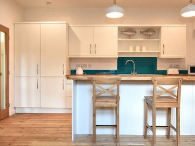 A kitchen with white cabinets a wooden floor and two wooden chairs at The Loft (Amble) in Amble