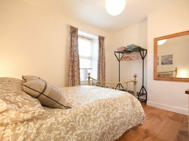 A bedroom with a metal bed frame patterned bedding a window with curtains a standing rack with towels and hangers and a large wall mirror at The Loft (Amble) in Amble