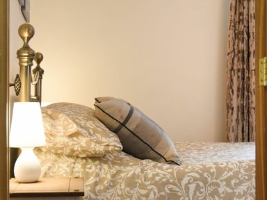 A bedroom with a bed with pillows and patterned bedding a bedside table with a lamp and patterned curtains at The Loft (Amble) in Amble