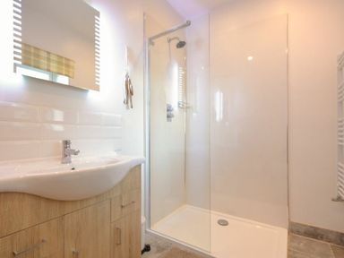 A bathroom with a wooden cabinet sink a glass shower enclosure and a wall-mounted mirror at The Loft Amble