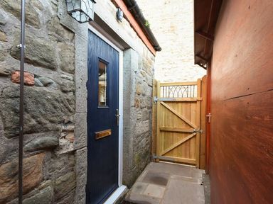 A narrow outdoor passage with a stone wall and blue door on one side and a wooden fence at the end at The Loft (Amble) in Amble