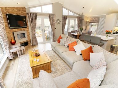 A living room with a large sectional sofa and wooden coffee table near a dining area at 8 Waterside Wood White Cross Bay near Troutbeck Bridge