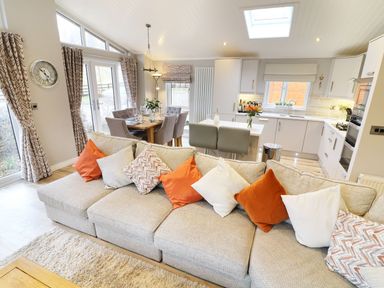 An open plan living room and kitchen with a beige sofa and dining table at 8 Waterside Wood White Cross Bay near Troutbeck Bridge