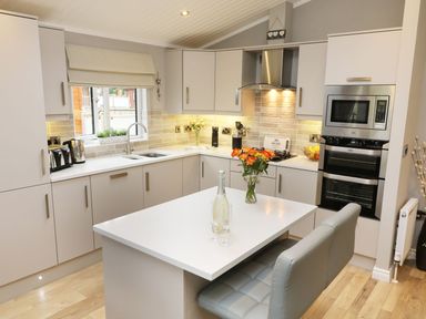 A kitchen with white countertops and cabinets a stove oven microwave and a dining table with chairs at 8 Waterside Wood White Cross Bay near Troutbeck Bridge