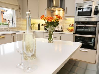 A kitchen with a white countertop island holding a bottle and two glasses and a vase of flowers at 8 Waterside Wood White Cross Bay near Troutbeck Bridge