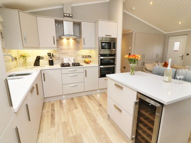 A kitchen with white cabinets cooking range and a small wine fridge at 8 Waterside Wood in White Cross Bay near Troutbeck Bridge