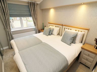 A bedroom with two single beds joined together bedside tables and a window with curtains at 8 Waterside Wood White Cross Bay near Troutbeck Bridge