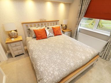 A bedroom with a double bed orange and silver pillows bedside tables and a window at 8 Waterside Wood White Cross Bay near Troutbeck Bridge