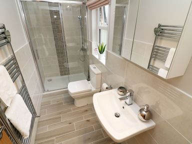 A bathroom with a shower, toilet, sink, towel rack, and a window with a plant at 8 Waterside Wood in White Cross Bay near Troutbeck Bridge