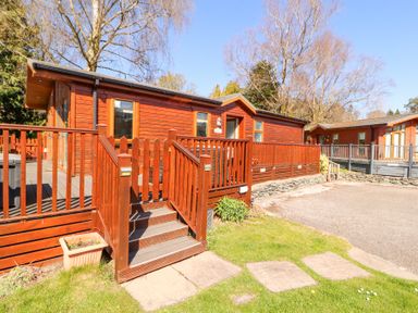 A wooden lodge with a deck and stairs in a grassy area at Bowness 66 in Troutbeck Bridge