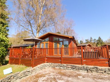 A wooden chalet with a fenced deck and umbrella on a sunny day at Bowness 66 in Troutbeck Bridge