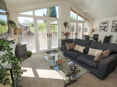A living room with a dark sofa glass coffee table tall windows and dining area at Bowness 66 in Troutbeck Bridge