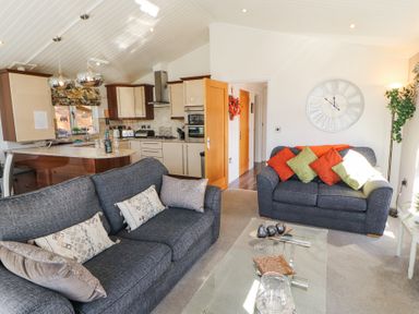 A living room with two sofas, cushions, a glass coffee table, a kitchen area with counters and appliances at Bowness 66 in Troutbeck Bridge