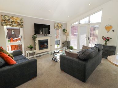 A living room with two dark sofas a glass coffee table and a TV above a fireplace at Bowness 66 in Troutbeck Bridge