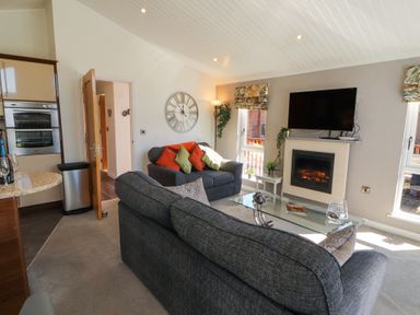 A living room with grey sofas a glass coffee table a wall-mounted TV and an electric fireplace at Bowness 66 in Troutbeck Bridge