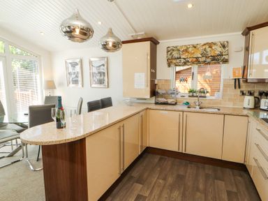 A kitchen with beige cabinets a granite countertop a dining table with chairs and hanging lights at Bowness 66 in Troutbeck Bridge
