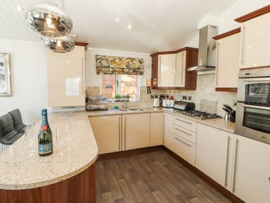 A kitchen with countertops cabinets a sink oven stove and a bottle of champagne with glasses at Bowness 66 in Troutbeck Bridge