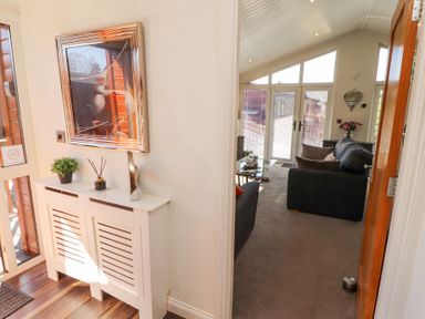 A hallway with a white cabinet and a square mirror next to a living room with sofas and a glass coffee table at Bowness 66 in Troutbeck Bridge