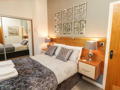 A bedroom with a double bed two bedside tables lamps and mirrored wardrobe doors at Bowness 66 in Troutbeck Bridge