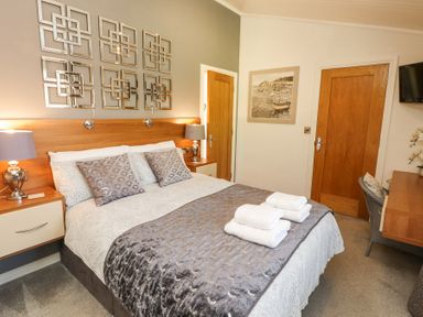 A bedroom with a double bed two bedside tables two lamps a wall mirror two doors and a desk with a chair at Bowness 66 in Troutbeck Bridge