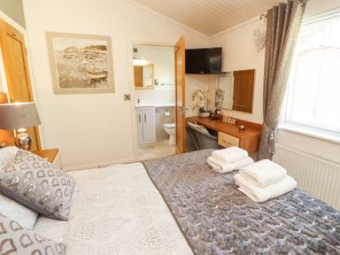 A bedroom with a bed folded towels a desk with a chair a wall mounted television and an open door to a bathroom at Bowness 66 in Troutbeck Bridge