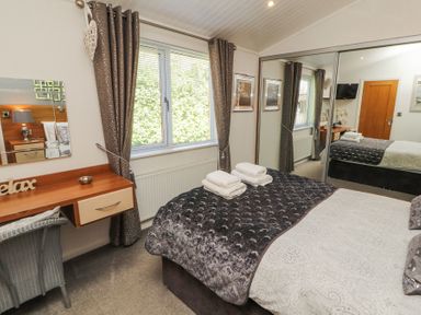 A bedroom with a bed with folded towels bedside table with mirror and chair and large wardrobe with sliding mirror doors at Bowness 66 in Troutbeck Bridge