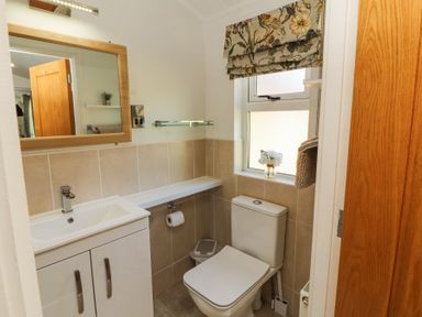 A small bathroom with a white sink cabinet a toilet a mirror a window with a floral curtain and a wooden door at Bowness 66 Troutbeck Bridge