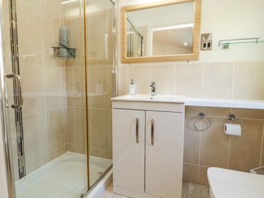 A bathroom with a shower enclosure, a white vanity with a mirror above it at Bowness 66 in Troutbeck Bridge
