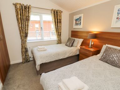 A bedroom with two single beds bedside table with lamp window with curtains and framed pictures on the wall at Bowness 66 in Troutbeck Bridge