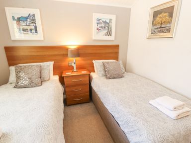 A bedroom with two single beds a wooden headboard a bedside table with a lamp and framed pictures on the walls at Bowness 66 in Troutbeck Bridge