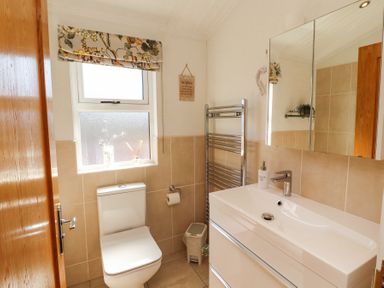 A bathroom with a toilet a sink with faucet a mirror above and a window with a floral curtain at Bowness 66 in Troutbeck Bridge