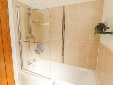 A bathroom with a bathtub shower combination and beige tiled walls at Bowness 66 in Troutbeck Bridge