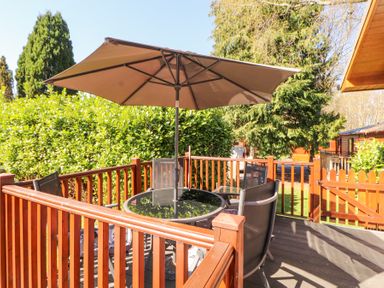 An outdoor deck with a round glass table and four chairs under a large umbrella at Bowness 66 in Troutbeck Bridge