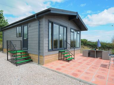 A small house with stairs leading to two doors and a patio with outdoor furniture and an umbrella at Midway Lodge in Cawsand near Kingsand
